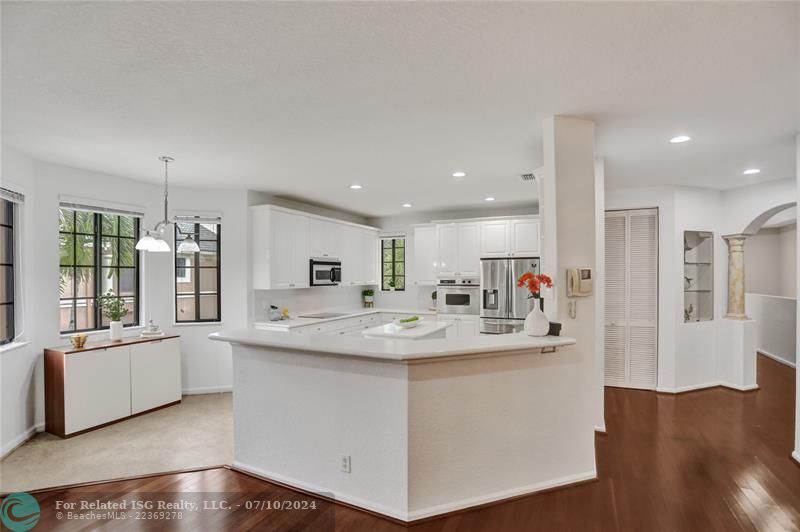 White kitchen with hi-hat lighting, tiled flooring and breakfast area, flanked by impact glass.