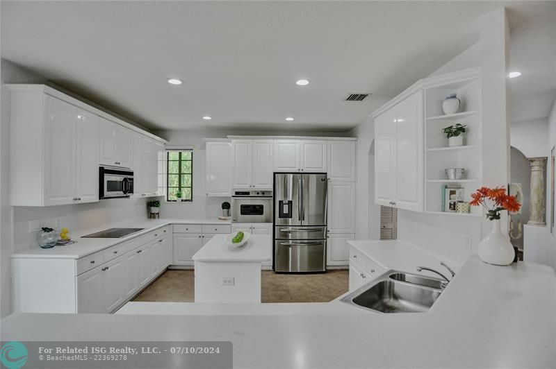 Sleek white cabinetry with crown molding, stainless appliances, display niche, stainless appliances and white corion countertops, create a timeless appeal.