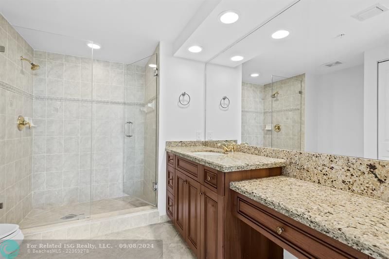 Spacious primary bath has frameless shower door, linen closet & vanity with granite countertops