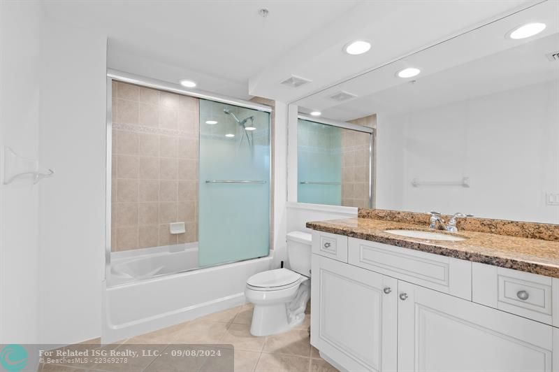 Guest bath features tub/shower combo, linen closet & modern white cabinetry with granite countertops