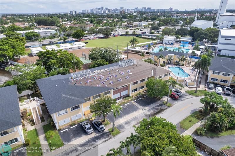 Aerial view with Fort Lauderdale Beach in the background.  New roof installation is being completed.  Large community pool and club area adjacent to building.