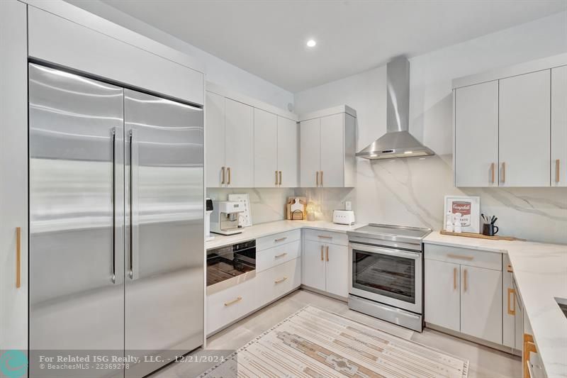 The kitchen features top-of-the-line JennAir stainless steel appliances and an elegant quartz countertop that extends as the backsplash.